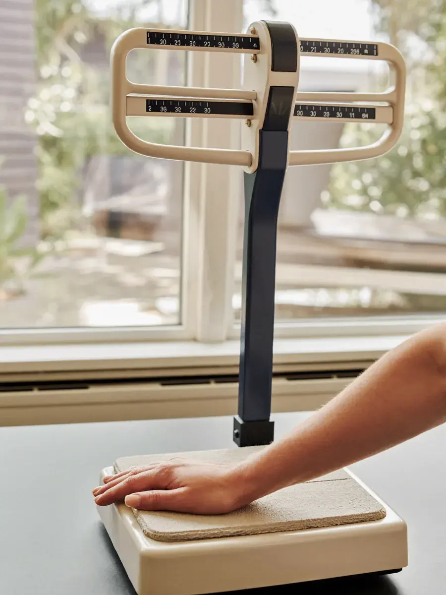 A hand resting on a medical balance-beam scale in a bright, calm clinic — Stilwell Wellness Solutions medical weight loss.